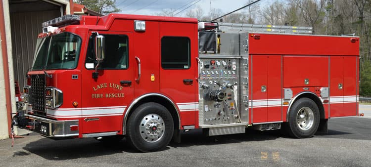 A red Lake Lure Fire Rescue engine parked beside a station bay, side view