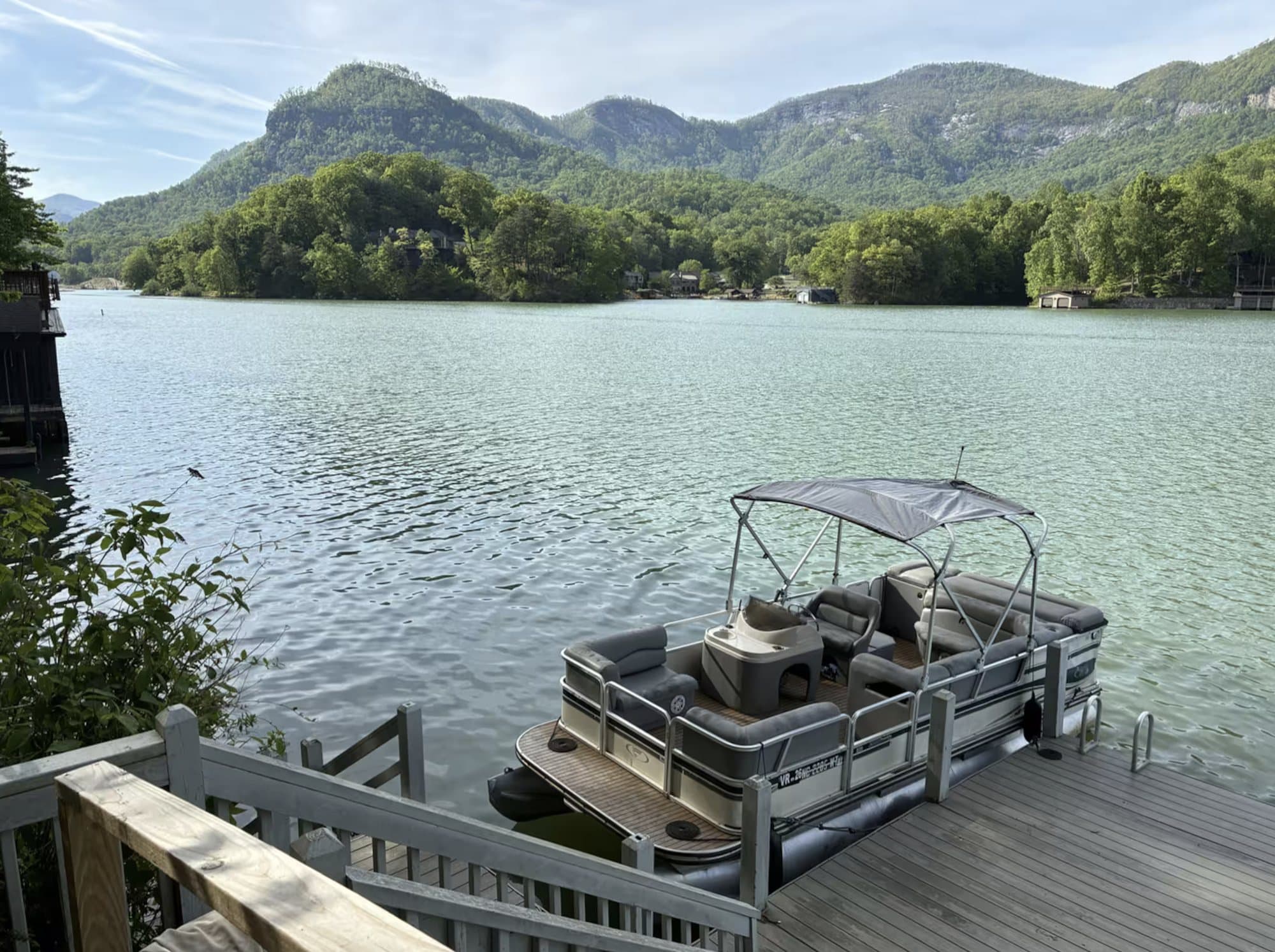 A pontoon boat tied to a wooden dock on Lake Lure with forested mountains and the lake behind it