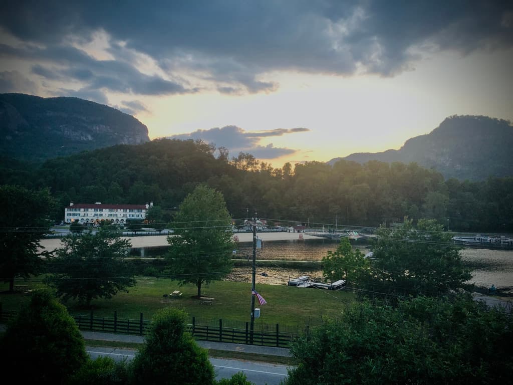 A dusk view of Lake Lure, NC, showing the Lake Lure Inn, docks, and boats on the water with the surrounding mountains in the background