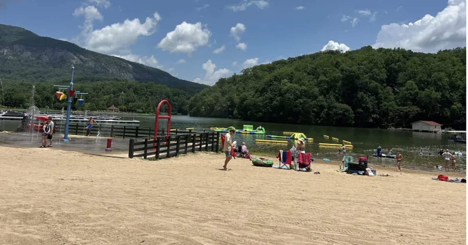 Lake Lure's public beach, with swimmers, a splash pad, and an inflatable obstacle course on the water, mountains in the background